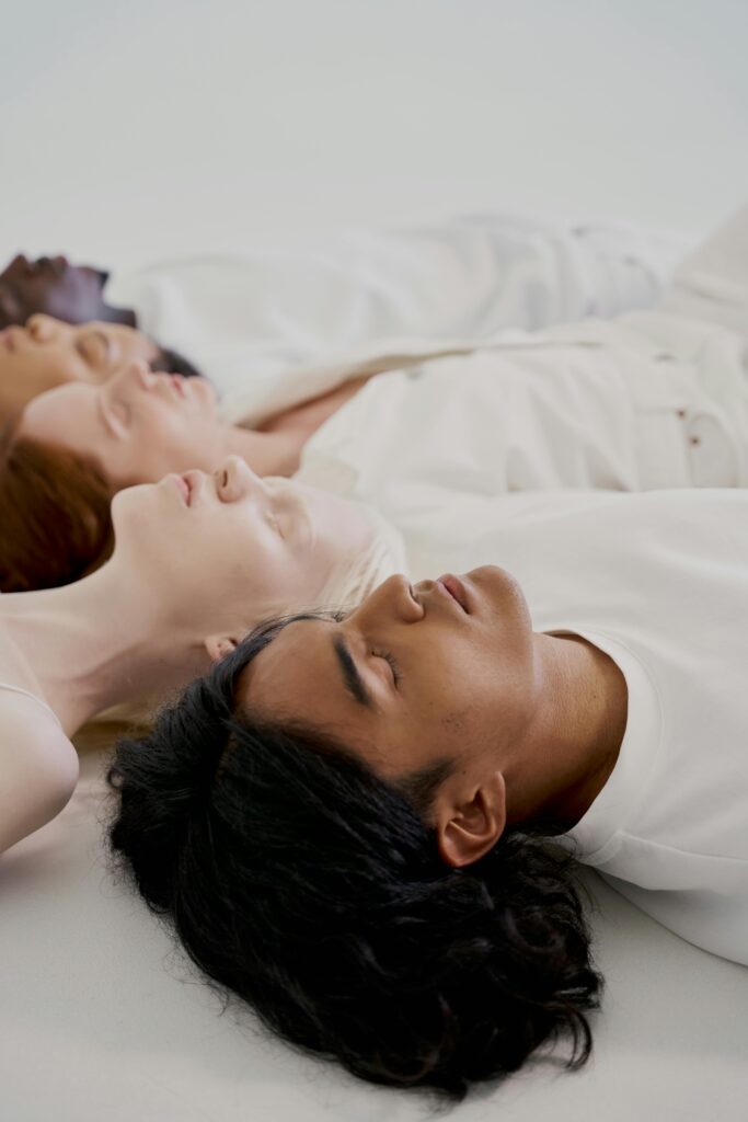 pexels-photo-10211656-10211656 Diverse group of individuals lying down with eyes closed on a white surface in a studio setting.